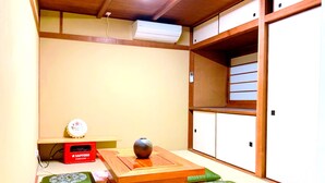 A traditional Japanese room with tatami flooring, a low wooden table, green cushions, a red box, and a ceiling-mounted air conditioner. - ONE Hostel Himeji (Himeji)
