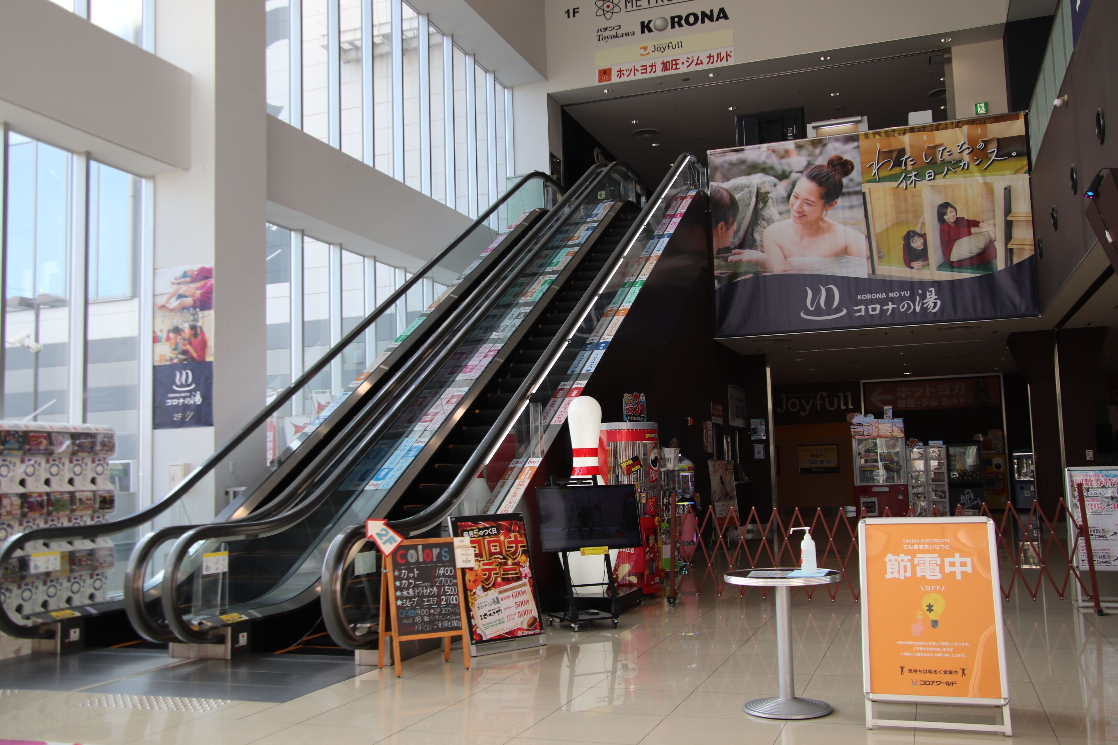 Un espace commercial intérieur doté d’escalators, d’un kiosque et d’une grande publicité.