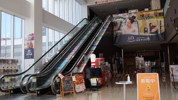 Un espace commercial intérieur doté d’escalators, d’un kiosque et d’une grande publicité.