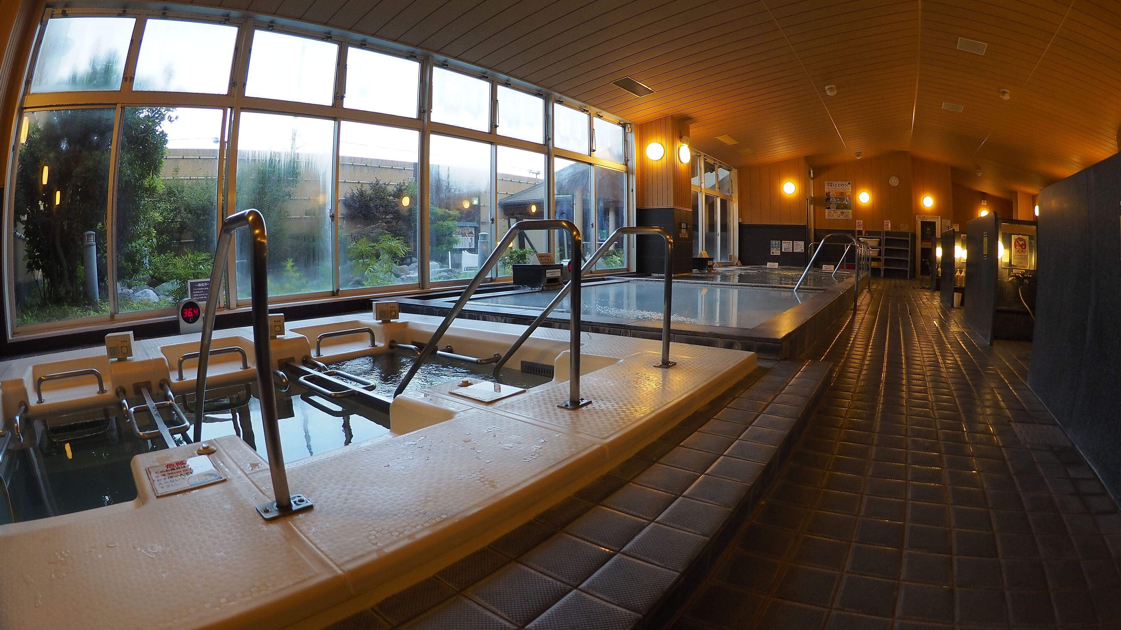 A large indoor swimming pool with multiple lanes, a changing room area, and a view of the outdoors through large windows.