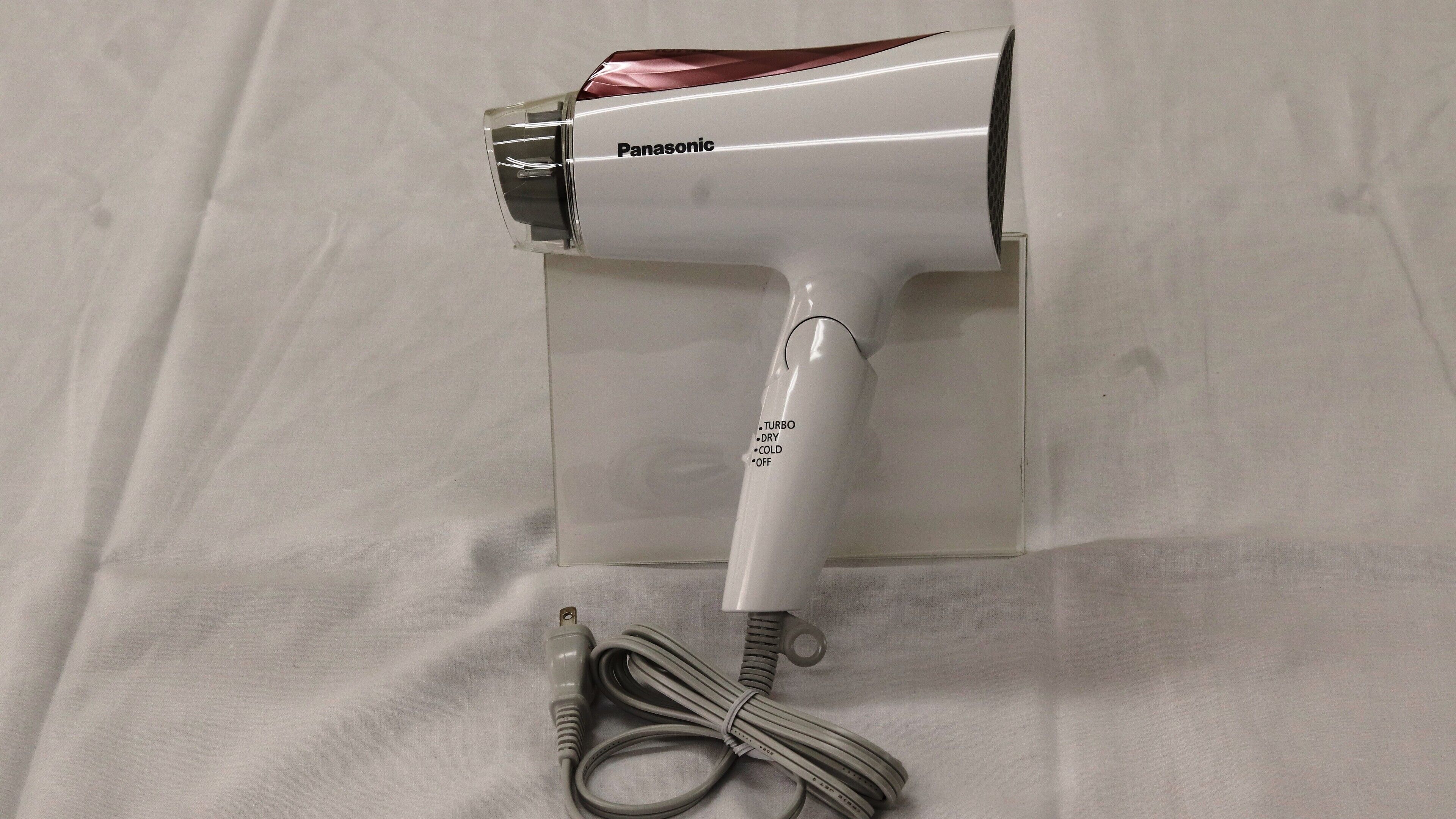 A Panasonic hair dryer with a cord and plug, placed on a white surface.