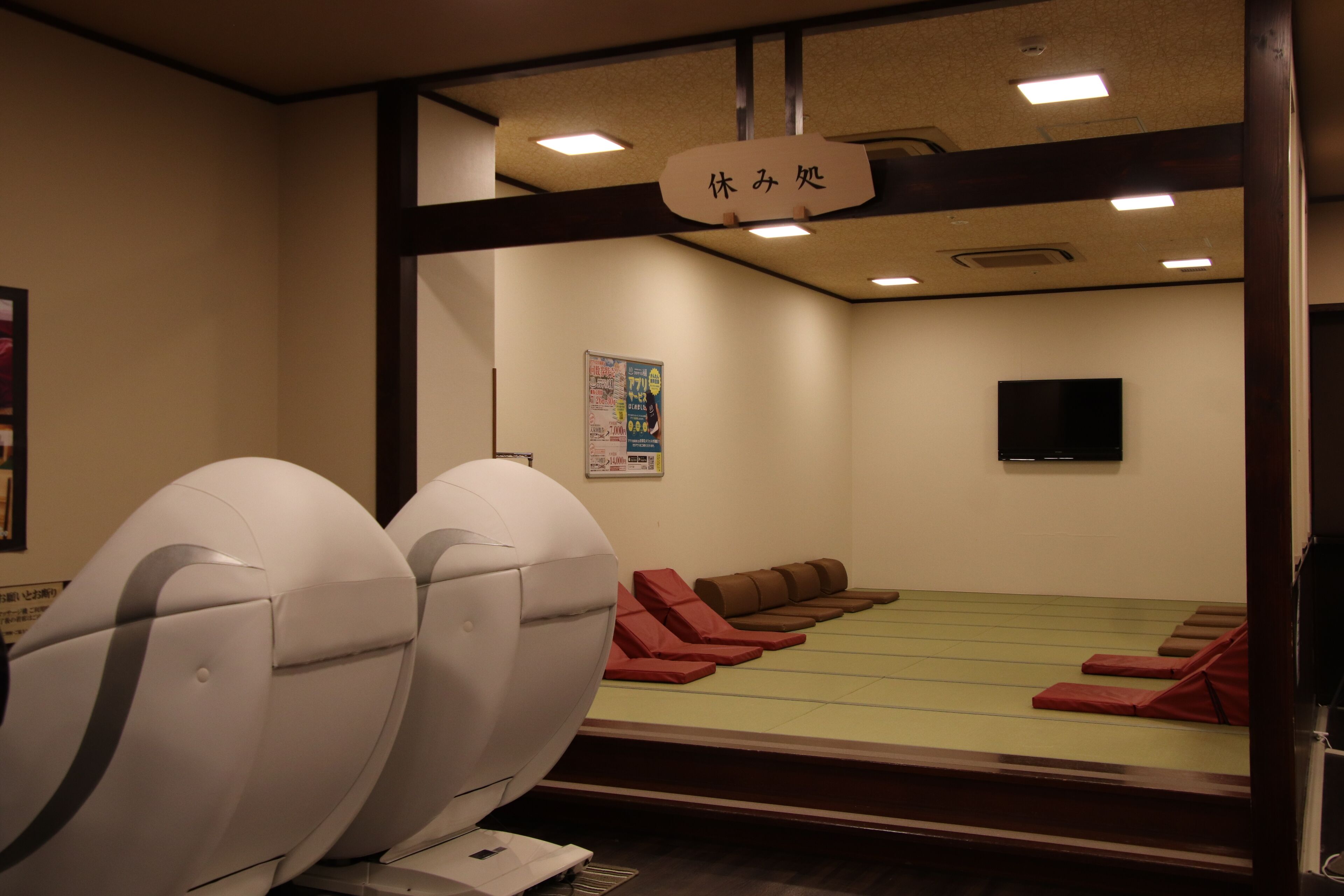 A room with massage chairs, a green massage table, and a sign with Japanese characters.