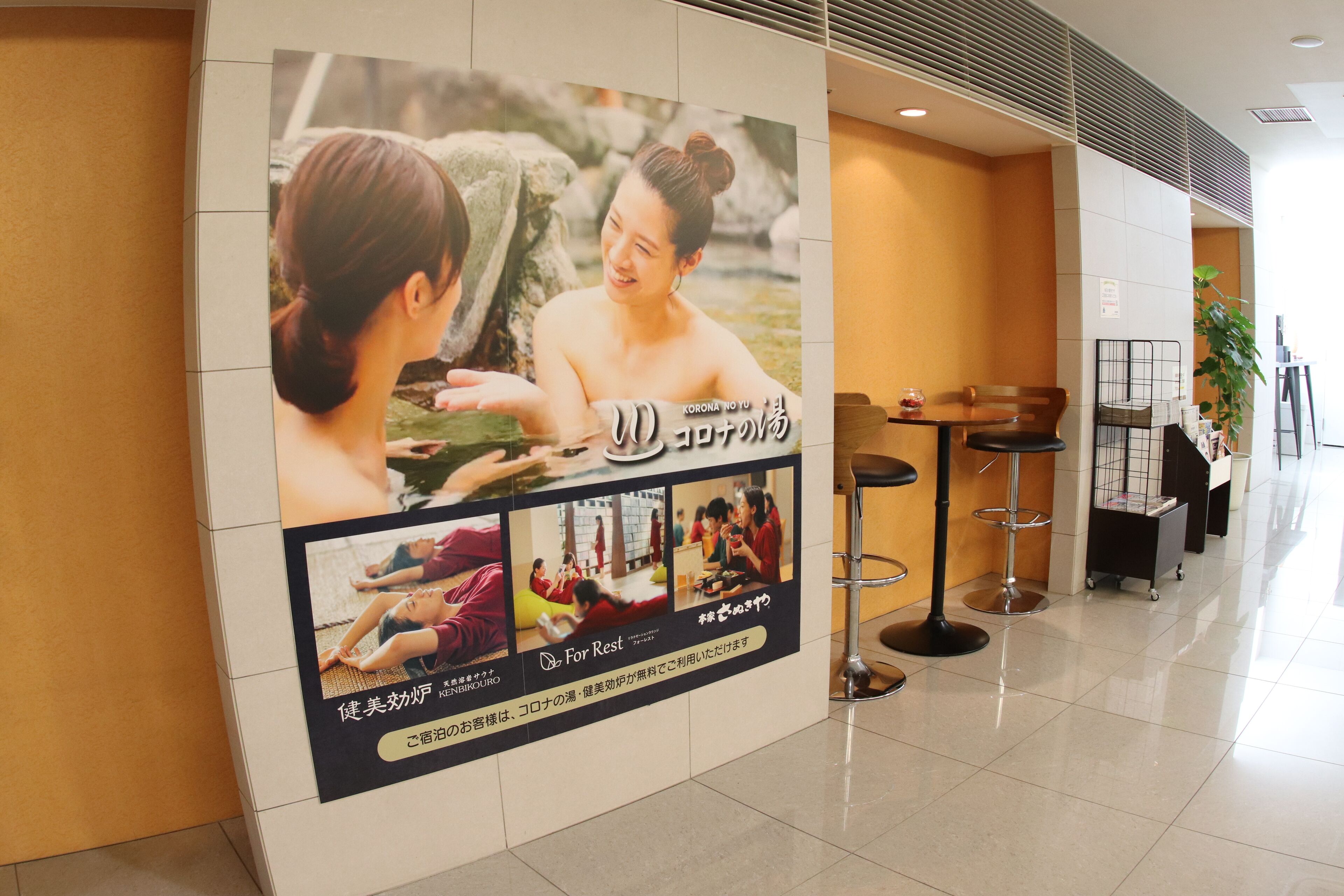 A hotel lobby with a large poster advertising a wellness program, a reception desk, and a seating area with tables and chairs.