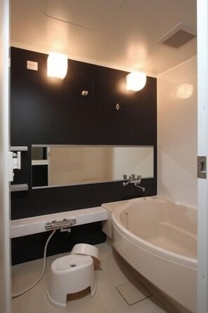 A modern bathroom with a large bathtub, a vanity with a mirror, and two wall-mounted lights. - Castle Inn Toyokawa (Toyokawa)