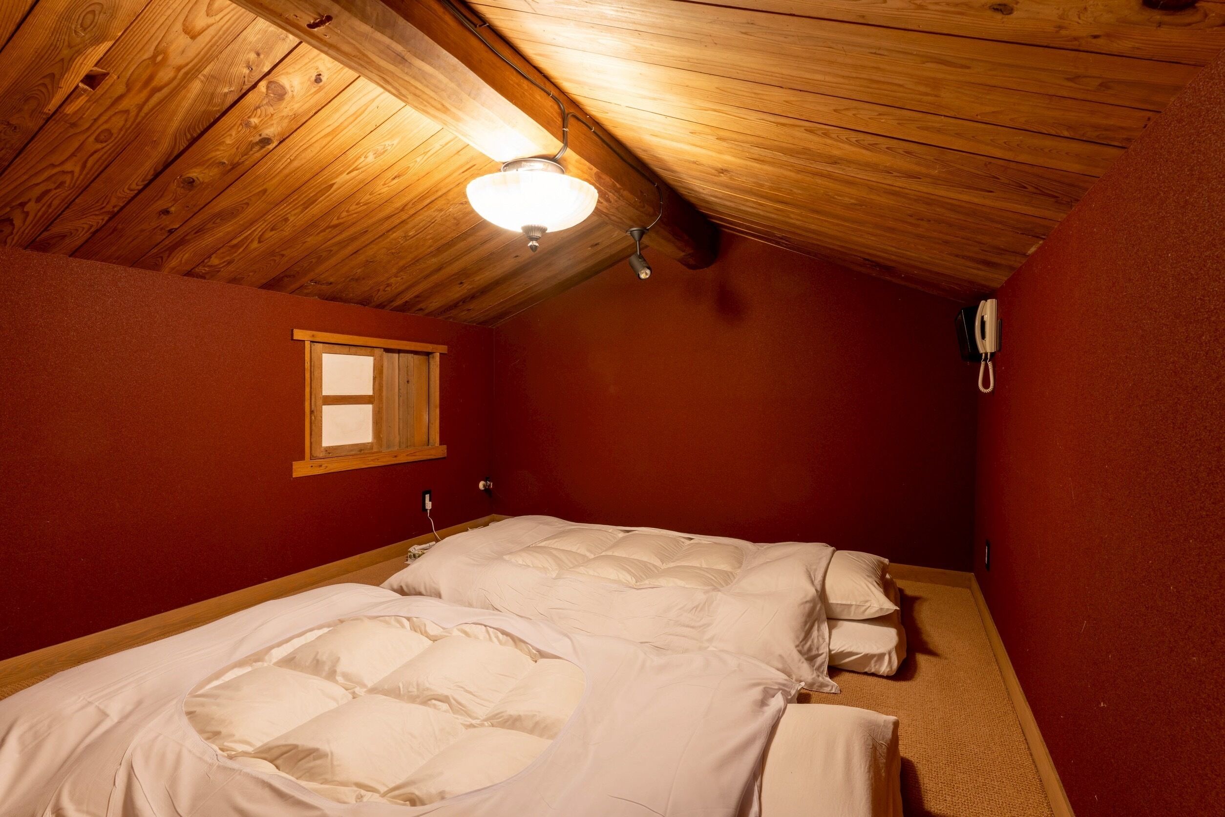 A bedroom with two beds, a wooden ceiling, a window, and a telephone.