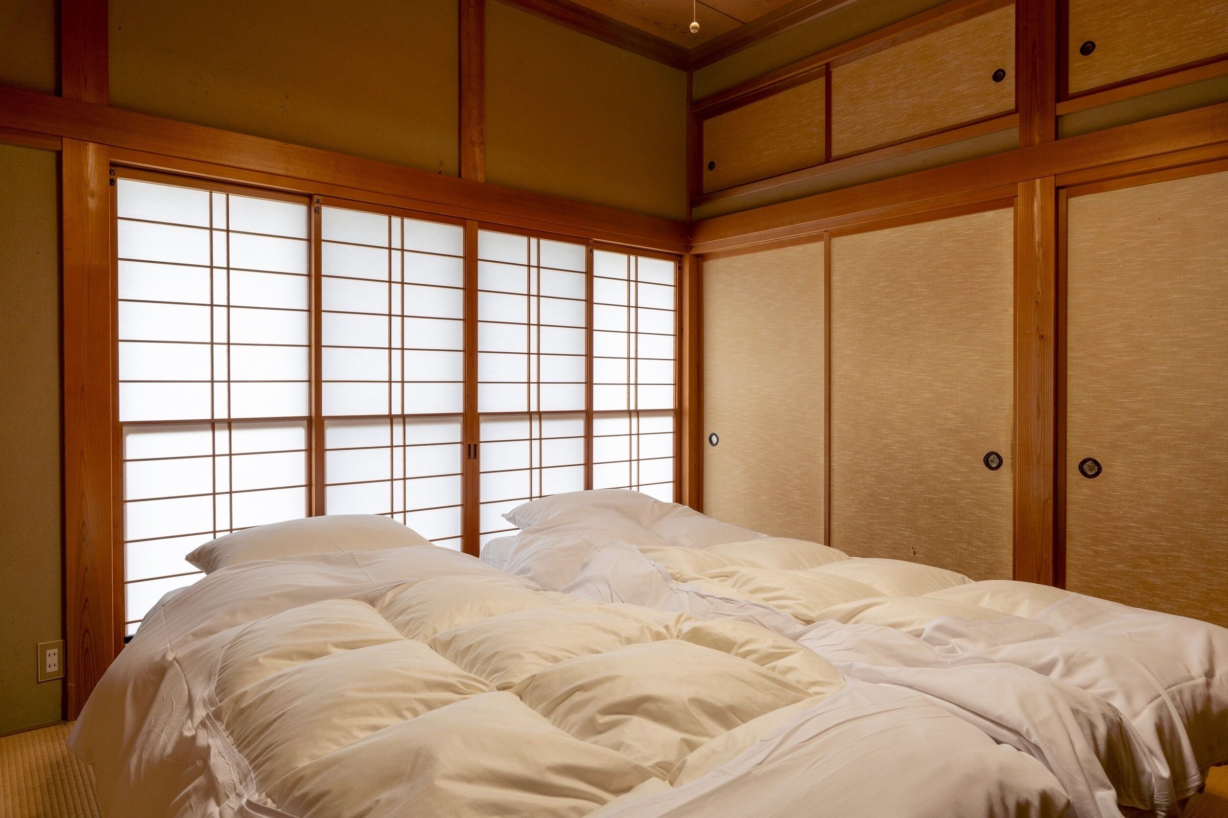 A traditional Japanese-style room with tatami flooring, a futon bed, sliding shoji doors, and a wooden ceiling.