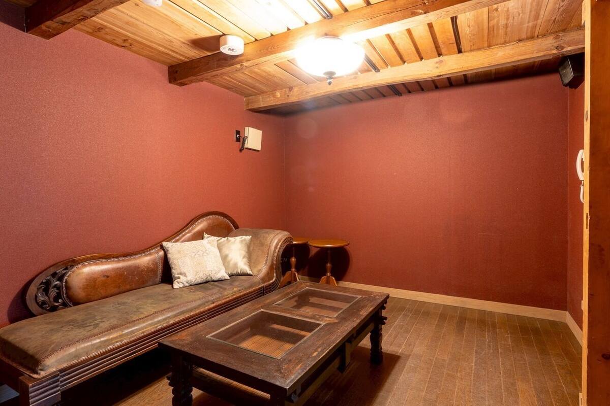 A room with a wooden ceiling, a red wall, a wooden bench, and a small round table.