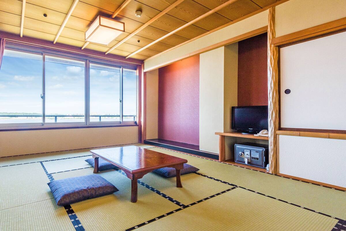 Una habitación con suelo de tatami, una mesa baja, cojines, un televisor y vista al agua.