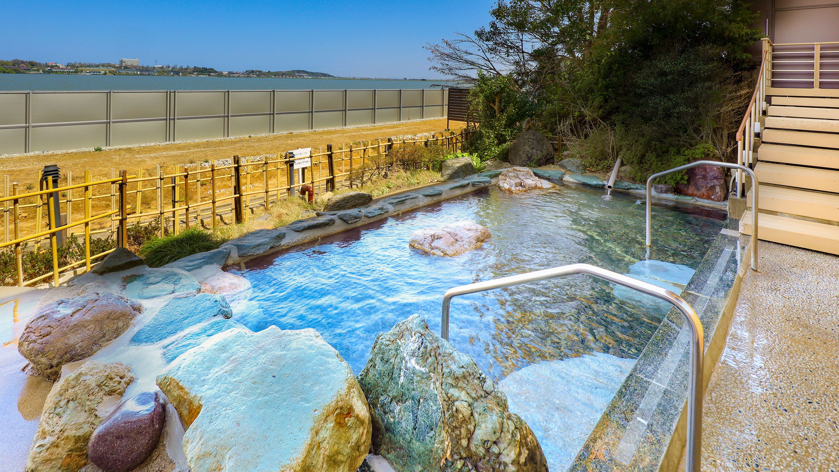 A hot spring area with a wooden deck, a stone pathway, and a view of the sea.