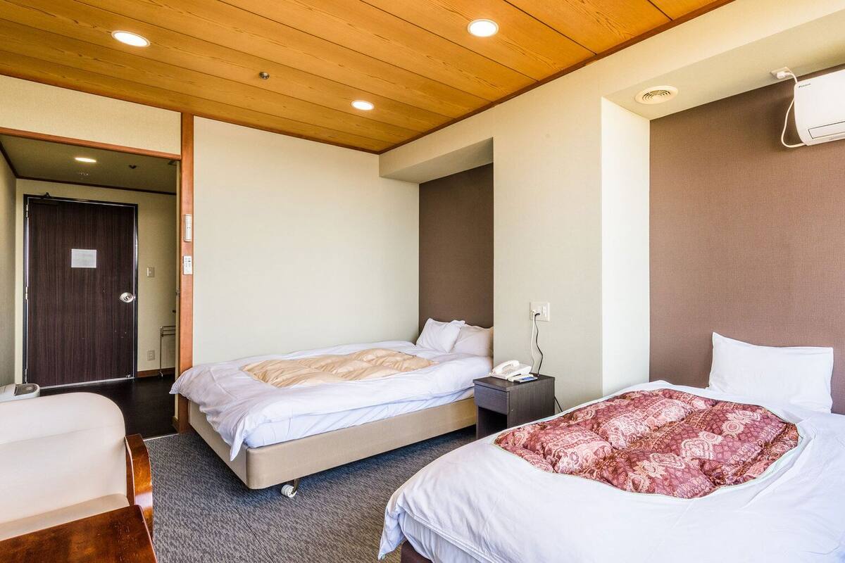 Una habitación de hotel con dos camas, techo de madera, aire acondicionado montado en la pared y una puerta.