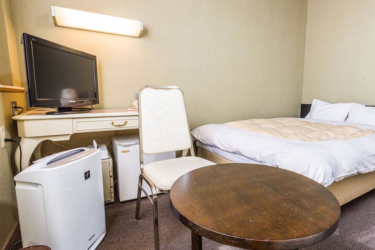 Ein Hotelzimmer mit Bett, Schreibtisch mit Computer, Stuhl, kleinem Kühlschrank und Tisch.