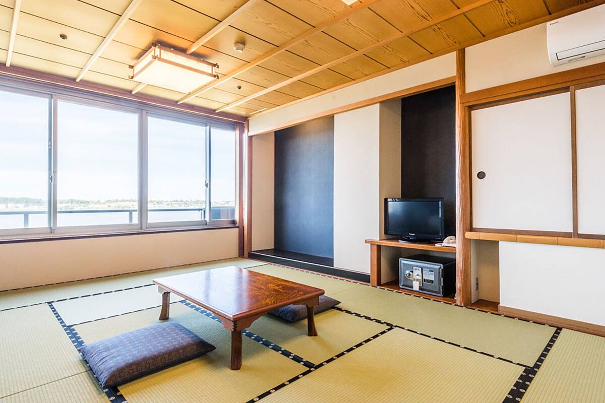 Una habitación con suelo de tatami, televisor, un mueble pequeño y un ventanal con vistas.