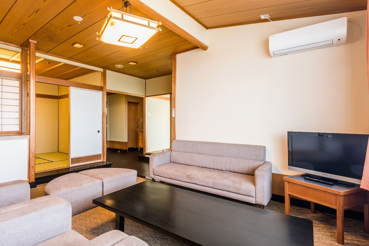 A traditional Japanese-style living room with tatami flooring, a sofa, a coffee table, and a television.
