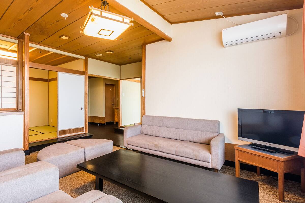 Una sala de estar tradicional japonesa con suelo de tatami, un sofá, una mesa de centro y un televisor.