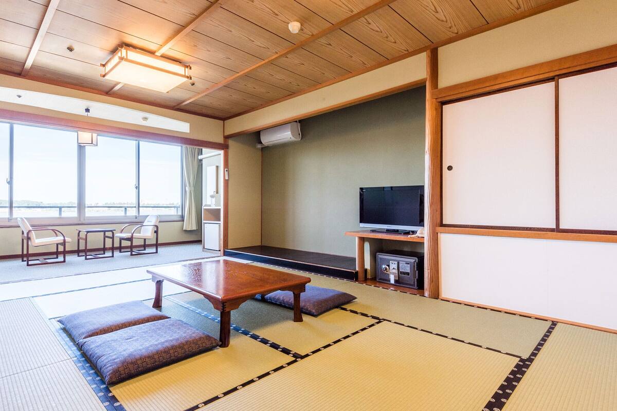 Una habitación tradicional japonesa con suelo de tatami, una mesita baja, un televisor y una puerta corredera.