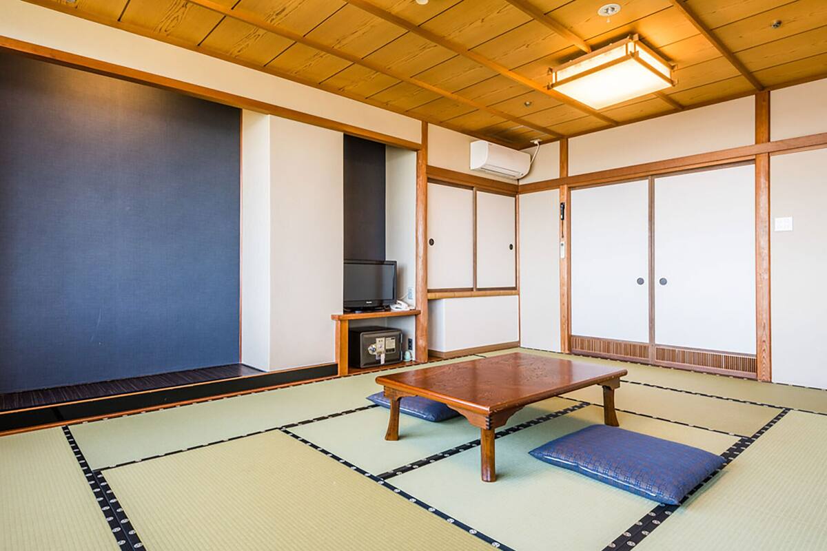 Una habitación japonesa tradicional con suelo de tatami, una mesa de madera baja, un televisor y puertas correderas.