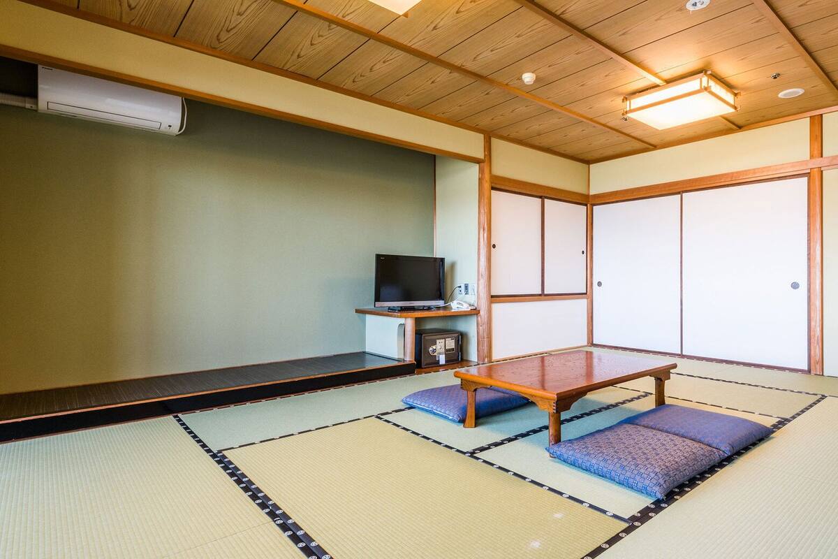 Ein Raum mit Tatami-Matten, einem Fernseher, einem kleinen Schrank und einer Heizung.