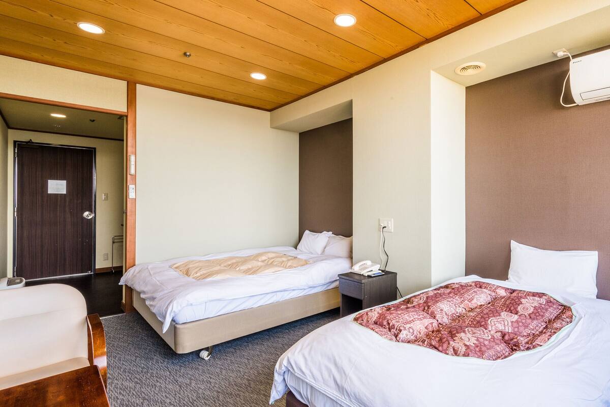 Habitación de hotel con dos camas, techo de madera, aire acondicionado instalado en la pared y teléfono junto a la cama.
