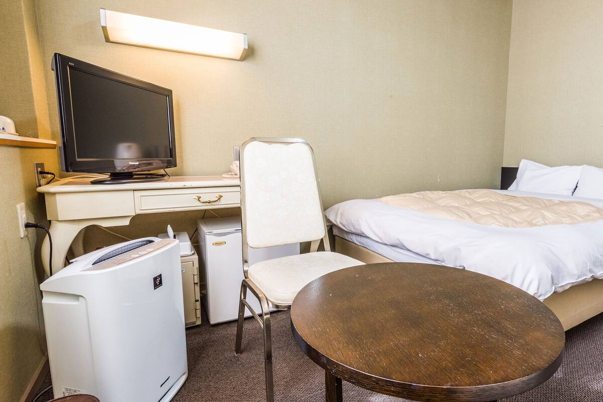 Habitación de hotel con cama, escritorio con televisor, silla, mesita y lavadora.