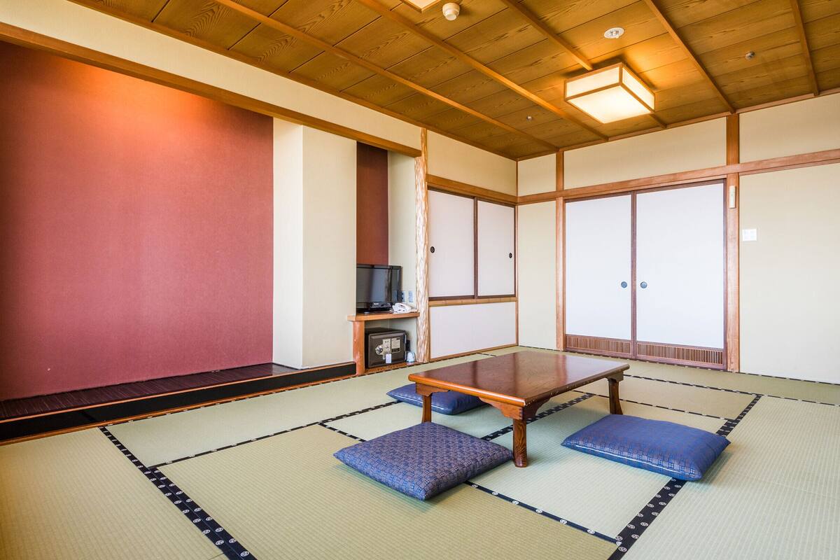 Una habitación japonesa tradicional con suelo de tatami, una mesa baja, cojines, puertas correderas y un televisor.