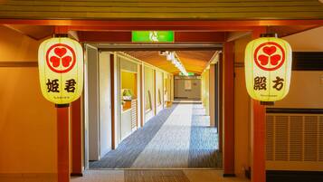 A hotel corridor with traditional Japanese lanterns, a clear exit sign, and a carpeted floor.