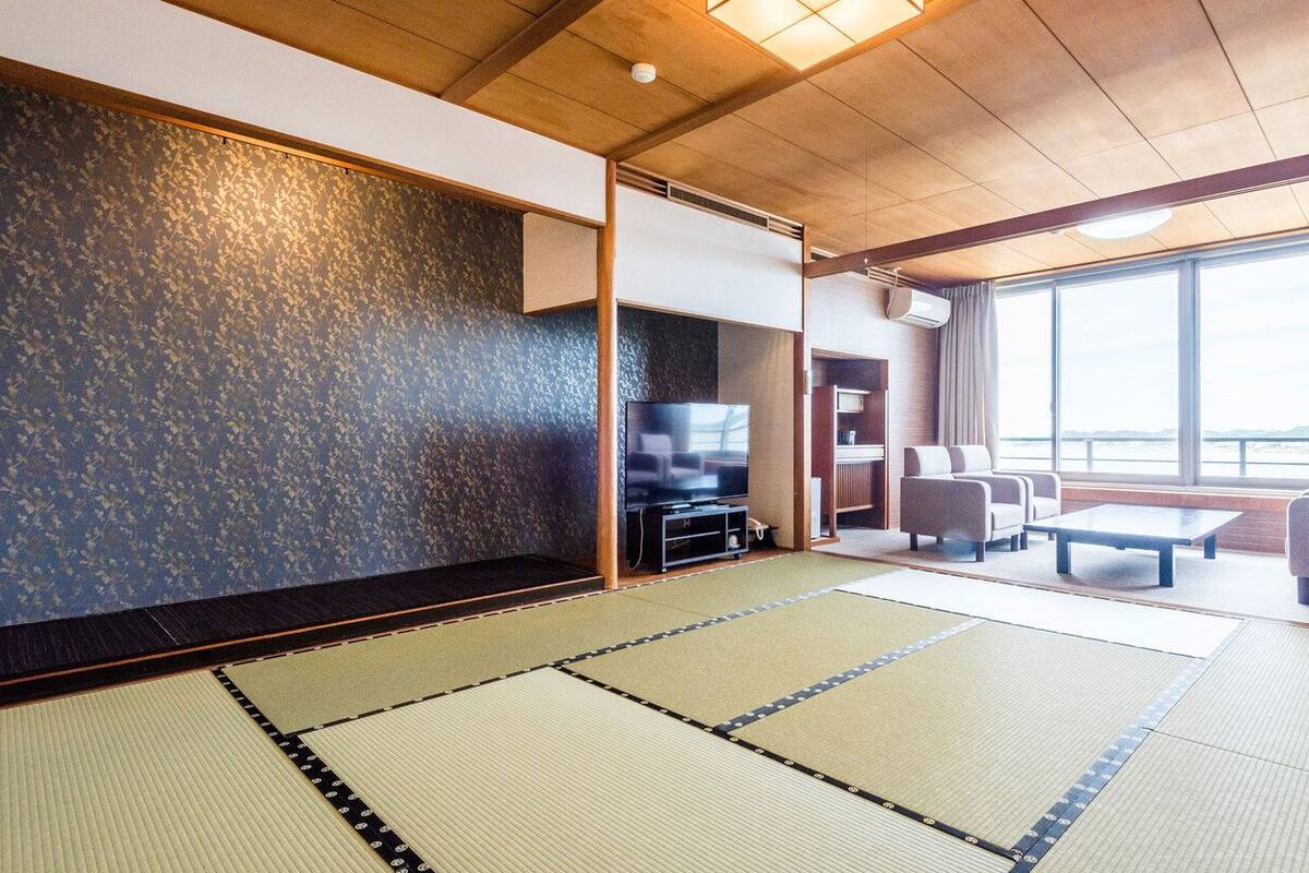 Ein Raum mit Tatami-Matten, ausgestattet mit Fernseher, Sofa und großen Fenstern.