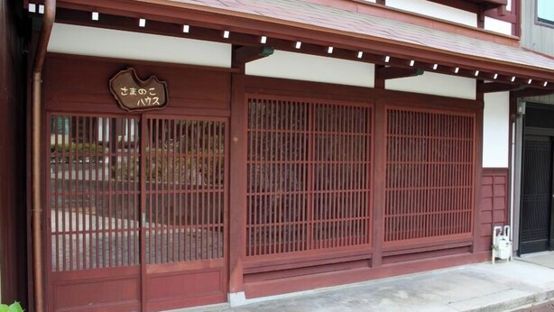 A traditional Japanese building with a wooden gate, a sign above the gate, and a concrete pathway leading to the entrance. - Samanoko House (Takaoka)