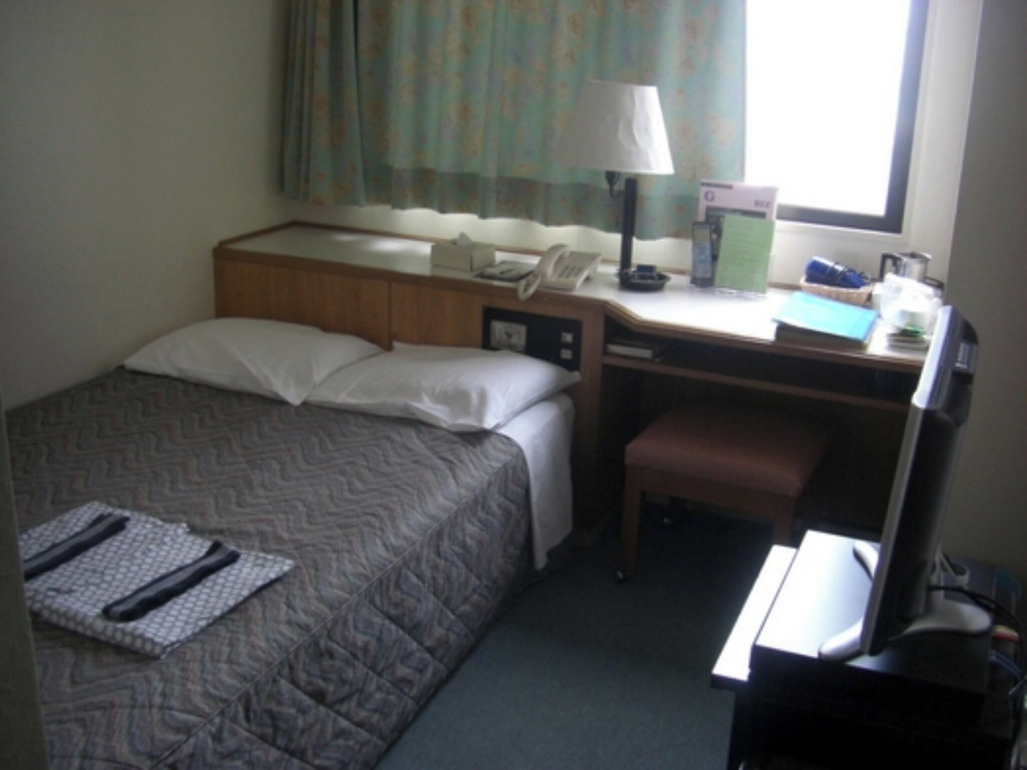 Habitación de hotel con cama, escritorio, silla, lámpara y ventana con cortinas.