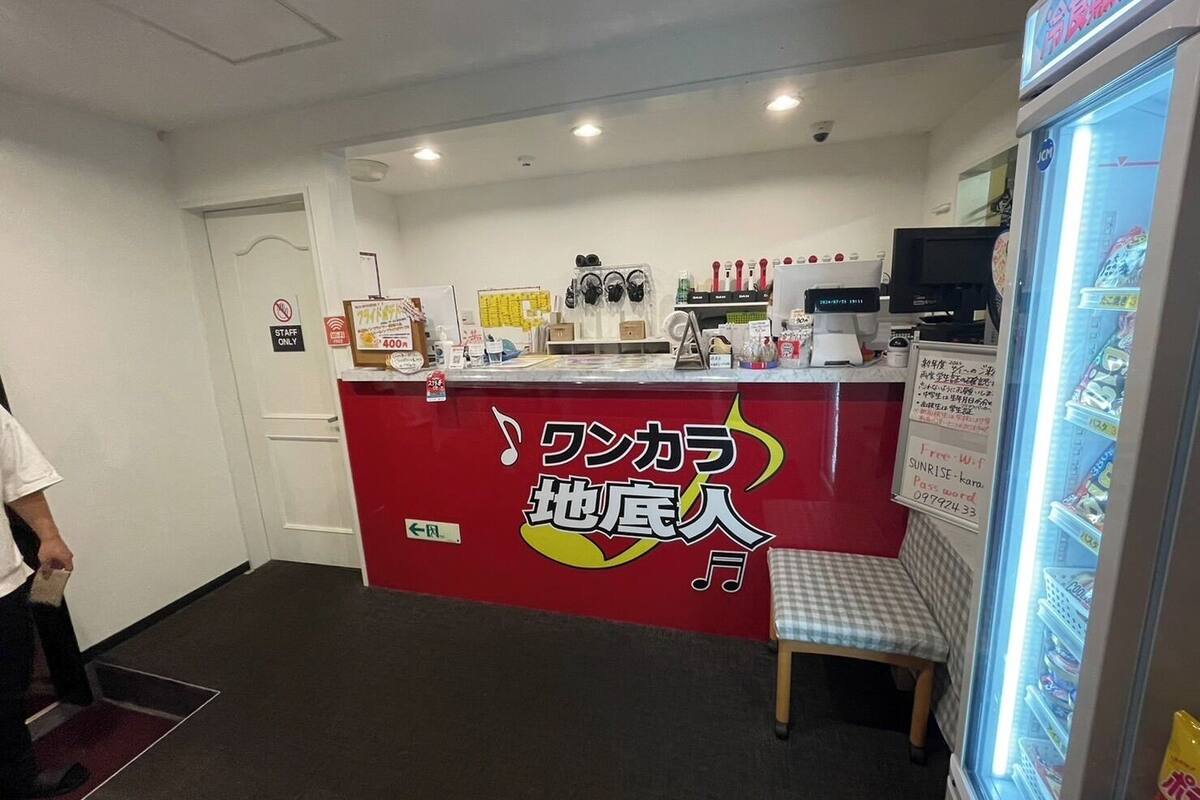 A reception area with a red counter, a seating bench, a refrigerator stocked with beverages, and a sign indicating Wi-Fi availability.