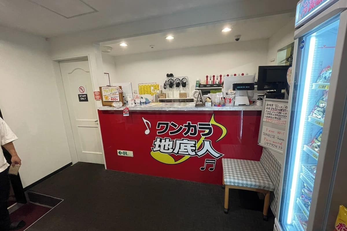 A reception area with a red counter, a seating bench, a refrigerator stocked with beverages, and a sign indicating Wi-Fi availability.