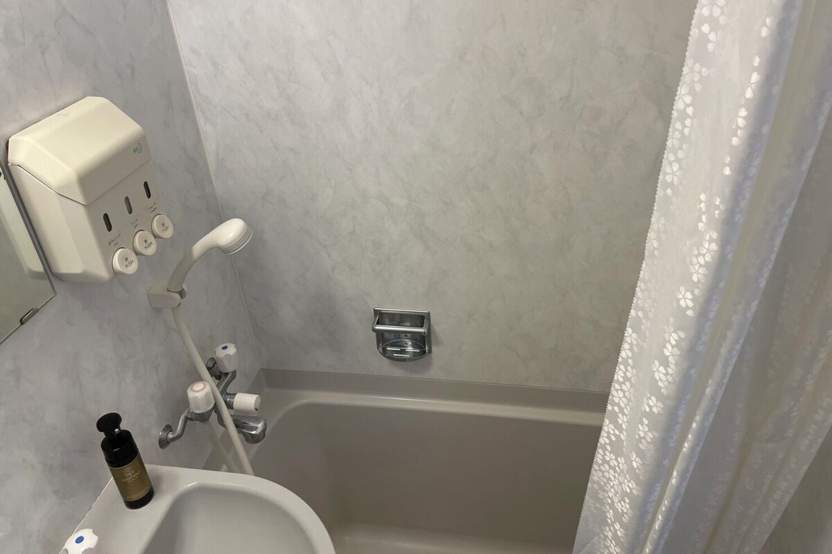 A bathroom with a bathtub, a hand soap dispenser, a bottle of shampoo, and a shower control panel.