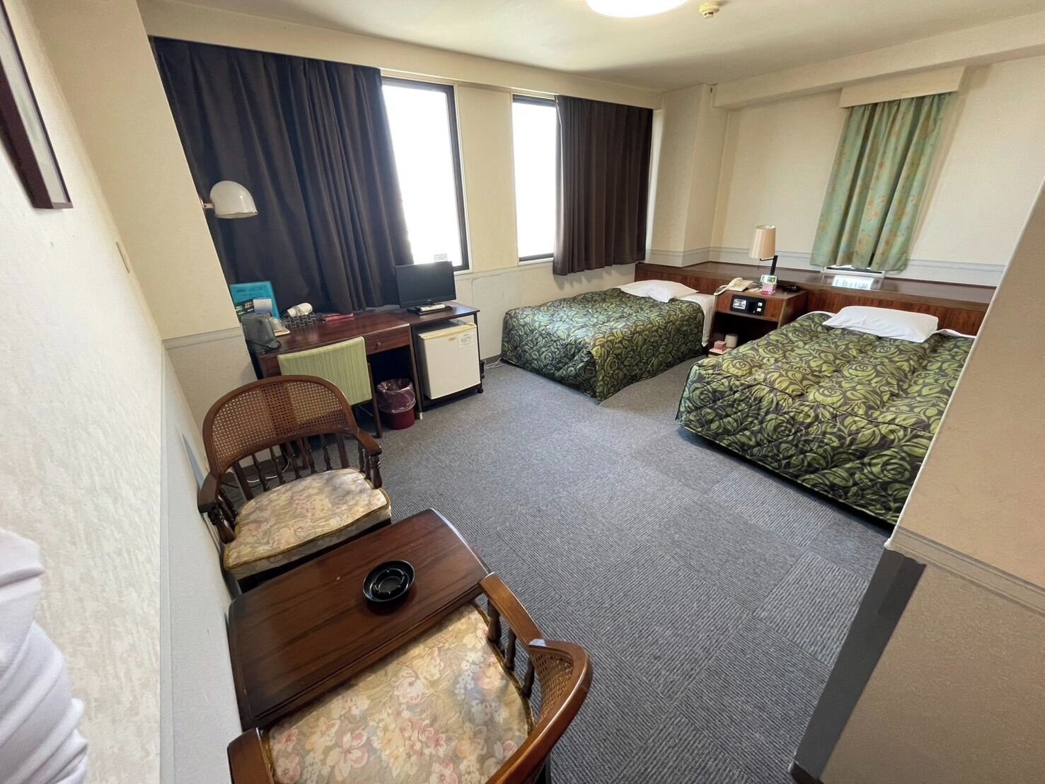 Una habitación de hotel con escritorio, dos camas, una silla, una mesita y televisor.