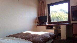 A hotel room with a bed, a desk, a television, and a window with a view of trees. - Hotel Nahari (Nahari)