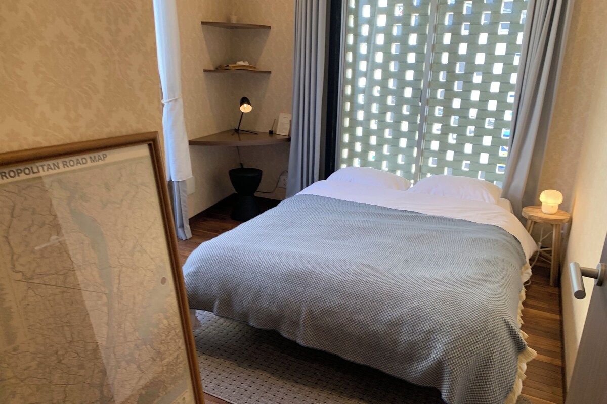 A bedroom with a bed, a map on the wall, and a window with a view of buildings.