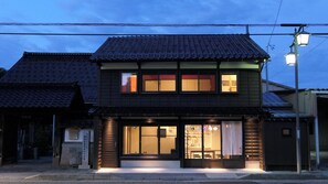 A traditional Japanese building with a tiled roof, large windows, and a well-lit entrance. - Teramachiya Fushin An (Kanazawa)