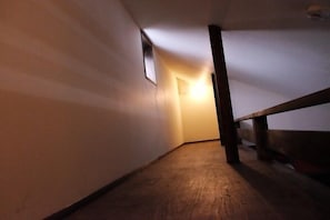 Un couloir étroit et faiblement éclairé, doté d’un plancher en bois et d’une rambarde en bois sur le côté droit.