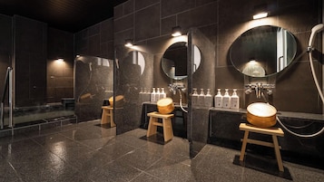 Un baño moderno con baldosas oscuras, taburetes de madera y una zona de ducha.