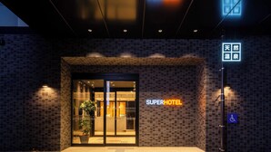 A hotel entrance with a neon sign, a wheelchair accessibility sign, and a potted plant outside. - Super Hotel Okayama Eki Higashiguchi Hot Spring (Okayama)