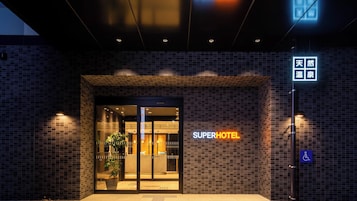 Entrada de hotel con letrero de neón, señal de accesibilidad para sillas de ruedas y una planta en maceta.