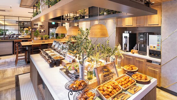 A buffet area with various food options, a coffee machine, and a kitchen in the background. - Super Hotel Okayama Eki Higashiguchi Hot Spring (Okayama)