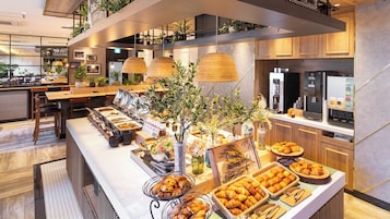 Zona de bufé con diversas opciones de comida, una máquina de café y una cocina al fondo.