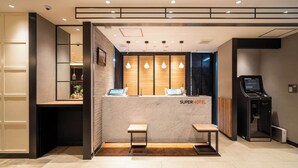 A reception desk with a digital screen, two small tables, and a seating area. - Super Hotel Okayama Eki Higashiguchi Hot Spring (Okayama)