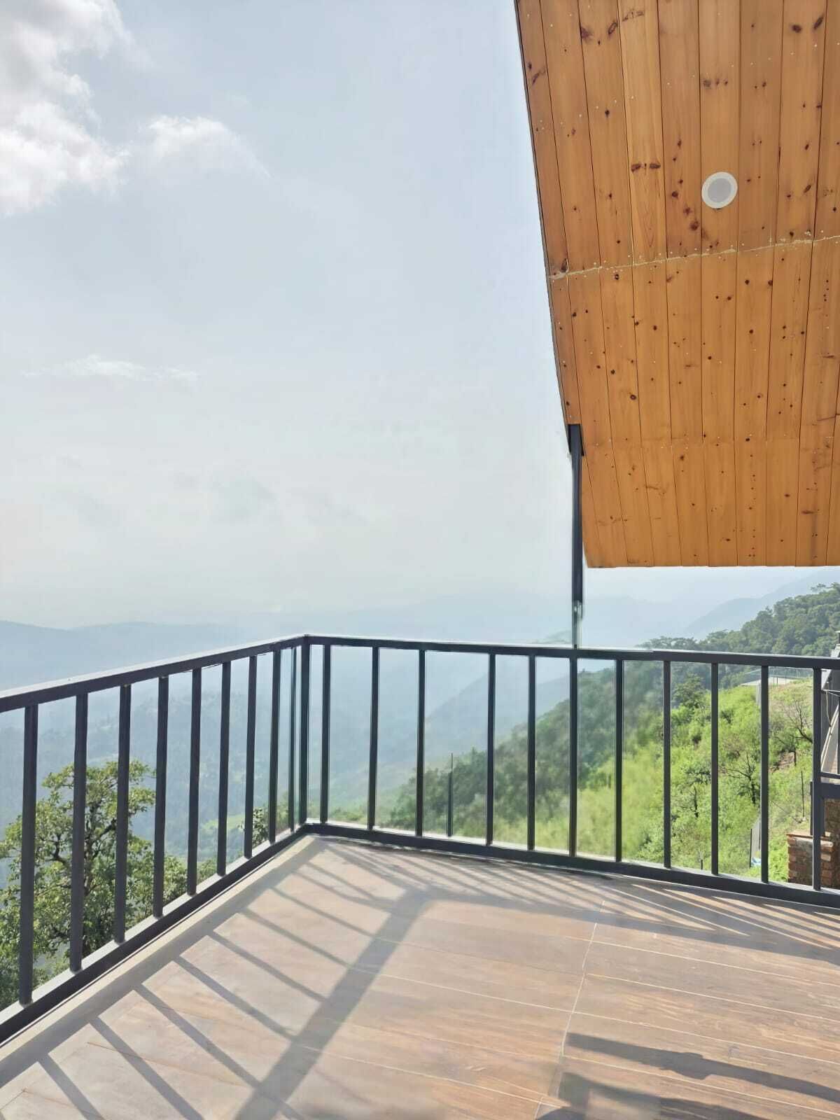 Un balcón con techo de madera y barandilla metálica, con vistas a un paisaje montañoso.