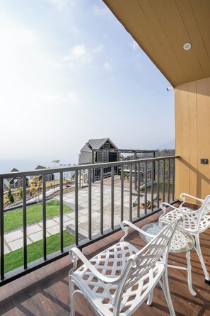 A balcony with white chairs and a view of a residential area. - Arkja Cottages (Vikasnagar)