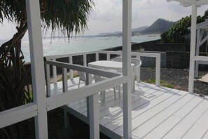 A white deck with a table and chairs, overlooking a body of water and hills.