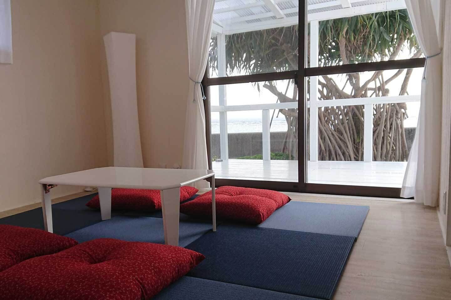 A room with a white table, red cushions, and a view of a tree through large windows.