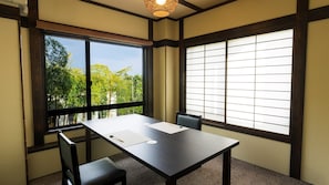 A room with a table and chairs, large windows with blinds, and a ceiling light fixture. - Gourmet Inn Izunohana (Ito)