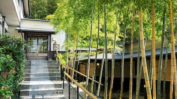 A traditional Japanese building with a staircase leading to a wooden door, surrounded by bamboo trees.