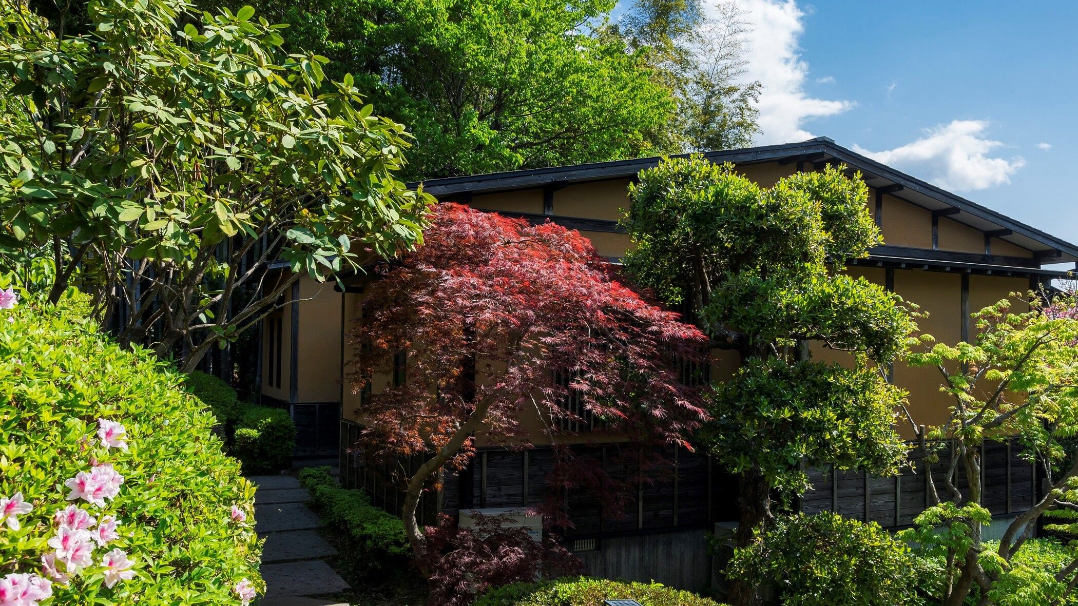 A traditional building with a sloped roof, surrounded by lush greenery and flowering plants.