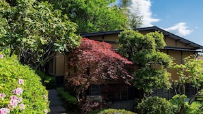 A traditional building with a sloped roof, surrounded by lush greenery and flowering plants. - Gourmet Inn Izunohana (Ito)